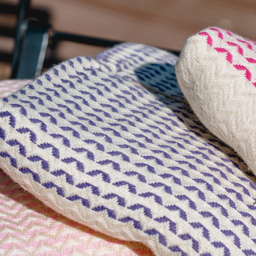 Ein tief violettes Ecobain Gordion Towel (Dark Lilac), das dekorativ um ein weißes, rundes Kissen gewickelt ist, mit sichtbarem Webmuster.