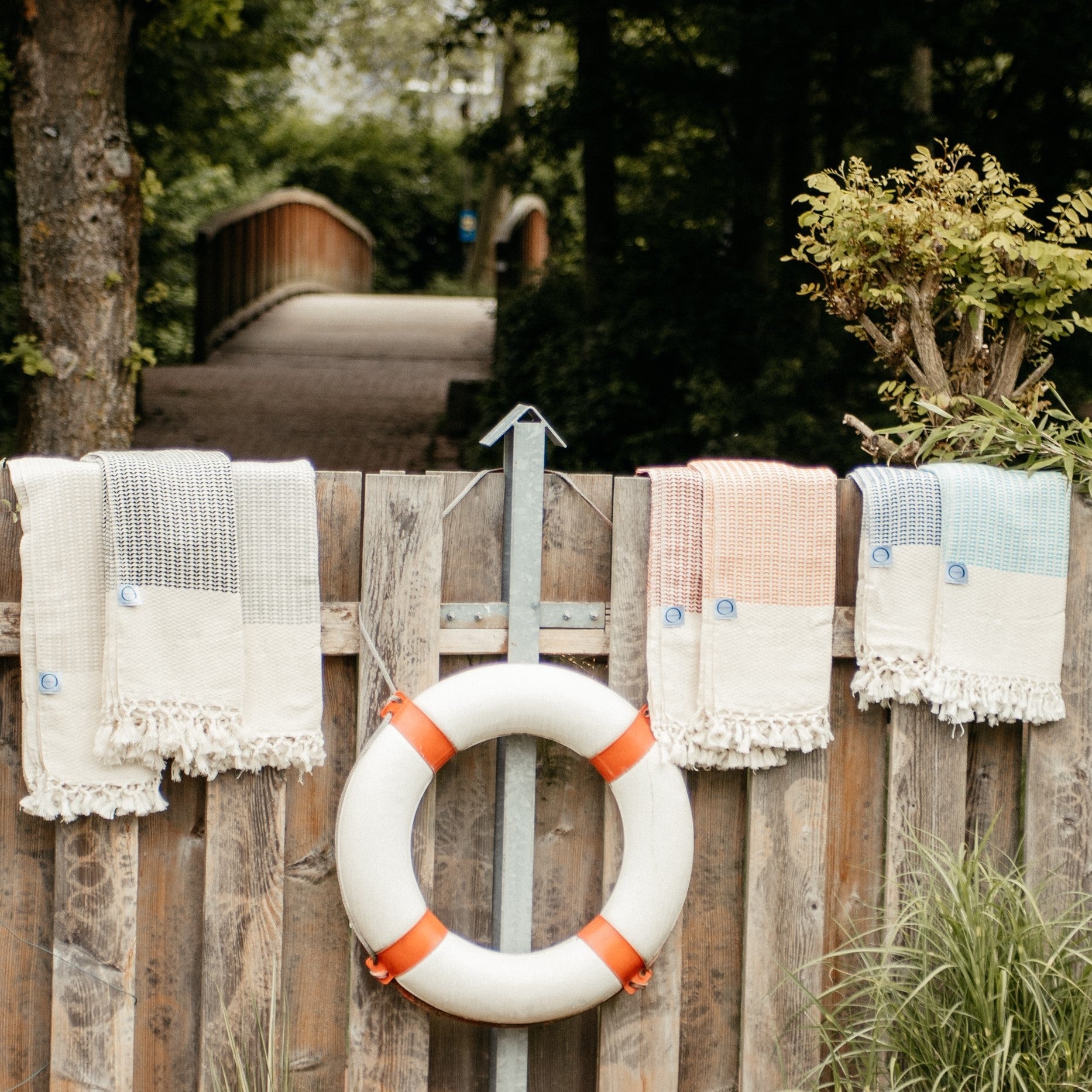 Flachliegende Anordnung der Ecobain Gordion Towel Kollektion in verschiedenen Farben (Blau, Grün, Beige) auf Holz.