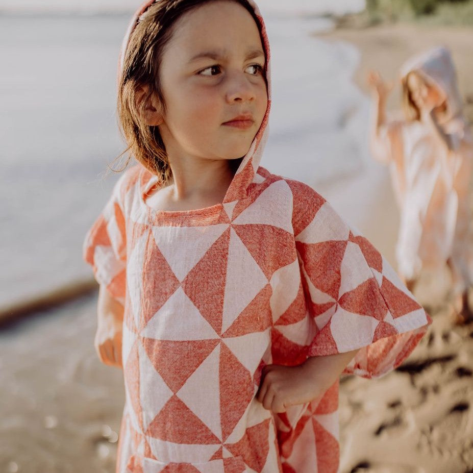 Eine Person trägt den saugstarken Ecobain Poncho Symique in Wild Cherry mit Kapuze, ideal als wärmender Überwurf nach dem Schwimmen.