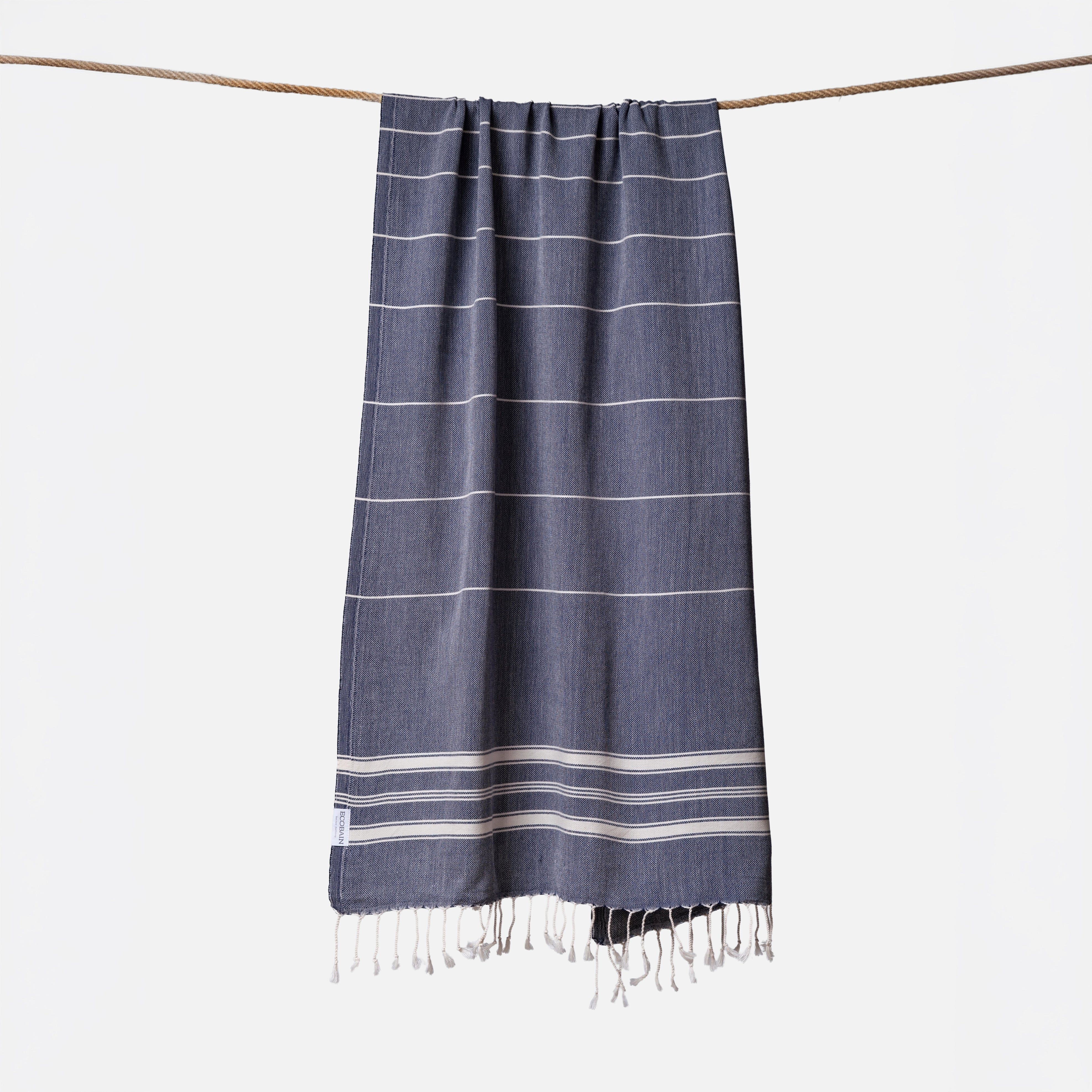 Extragroßes Ecobain Strandlaken der Liberty Series im minimalistischen Design Midnight Anchor. Das platzsparende Pestemal in 100x200 cm wird stilvoll gerollt mit originalem Hang Tag geliefert und ist die ideale nachhaltige Geschenkidee für aktive Familien. Ein absolut sandfreies Reisehandtuch aus pestizidfreiem Anbau, das selbst bei großem Gepäck für die ganze Familie die Badetasche federleicht hält und schweres Frottee ersetzt.