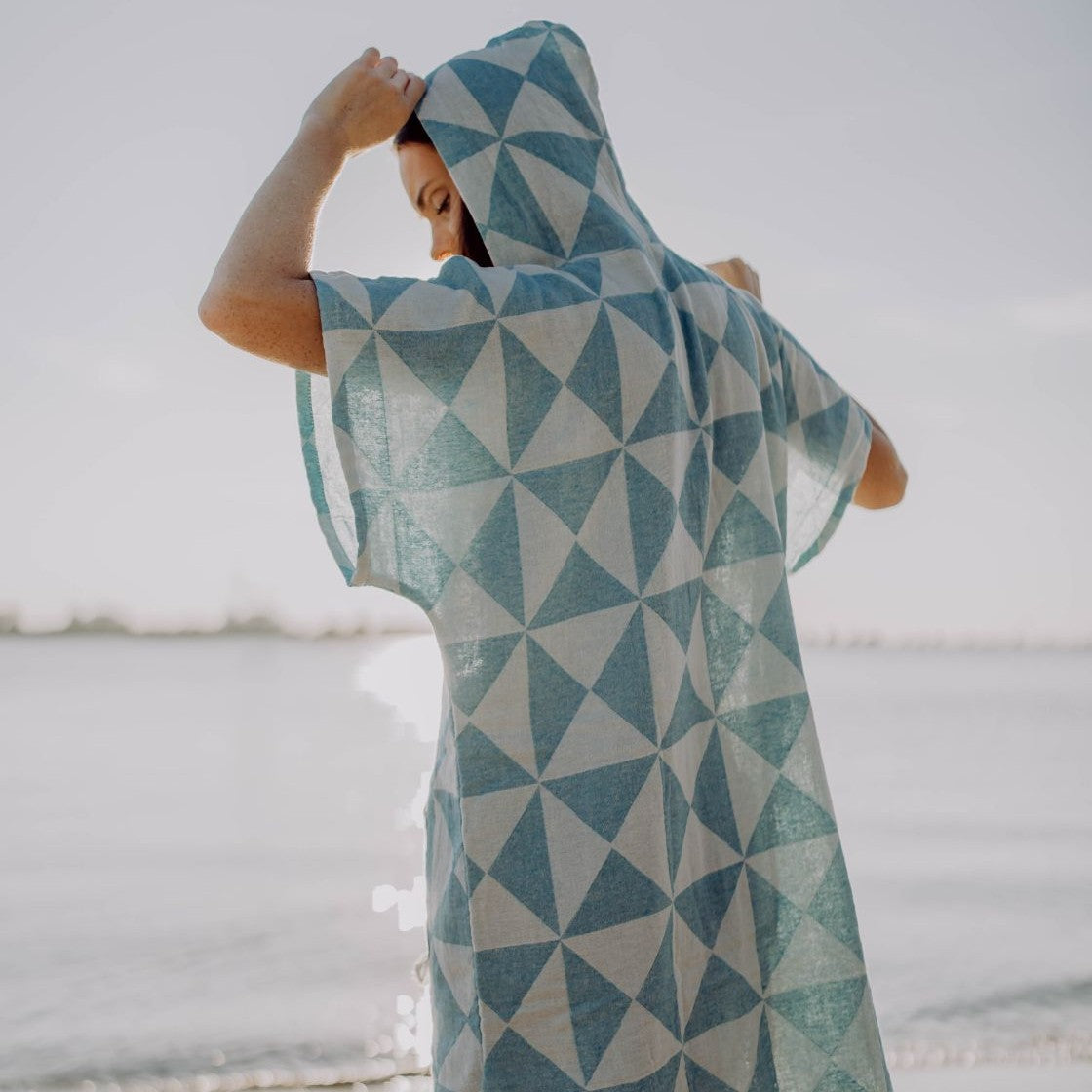 Eine Person spaziert fröhlich im Freien und trägt den Ecobain Poncho Symique in maritimem Blue Hawaii mit aufgesetzter Kapuze.