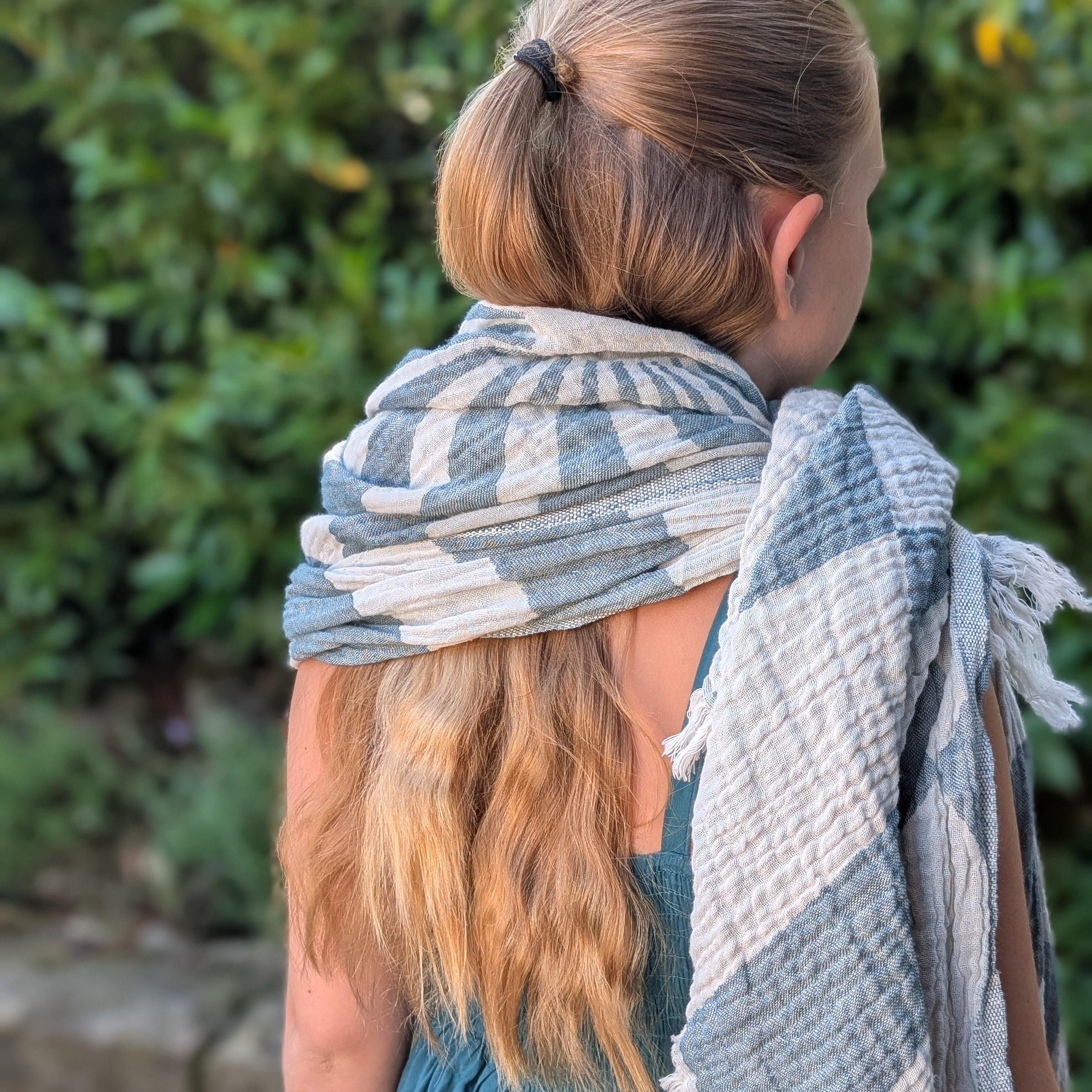 Detailaufnahme eines Ecobain Hammamtuchs im Design 'Sailor's Dream' mit charakteristischem radialen Streifenmuster. Das Tuch aus nachhaltigen Naturfasern schmiegt sich leicht um die Schultern eines Kindes, Akzent auf der weichen, taktilen Webstruktur und handgeknüpften Fransen